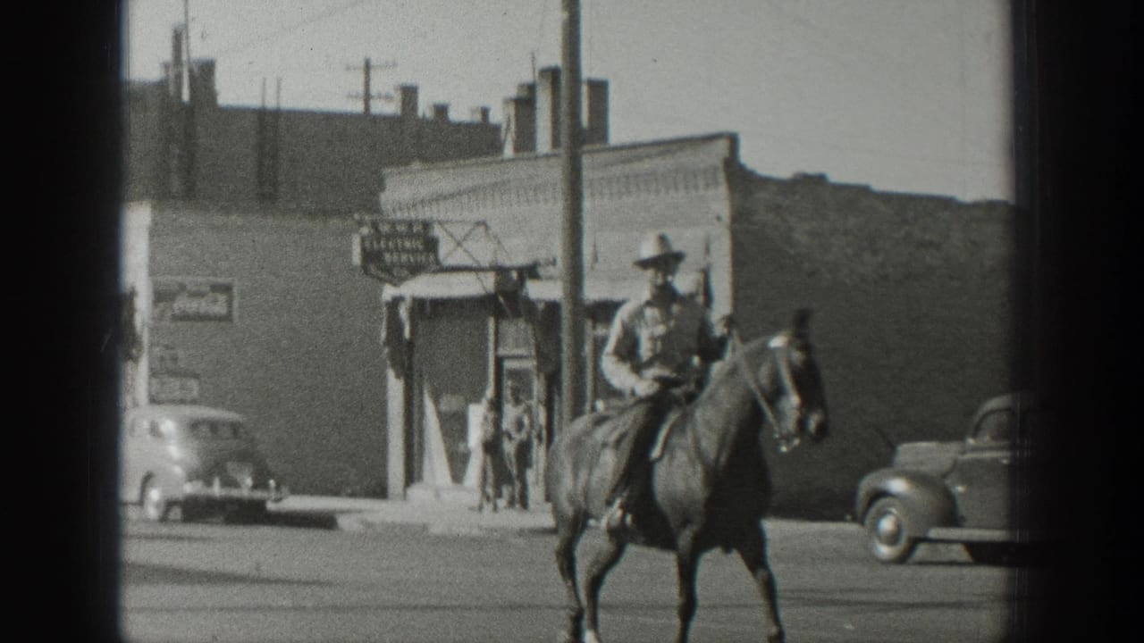In 1939 Wyoming home-movie footage, a mounted man rides along a main street with storefronts, parked cars, and a signboard behind him.