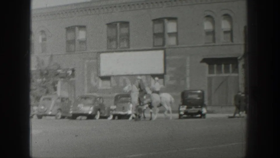 Mounted riders on a Wyoming street appear near classic parked automobiles and a brick commercial facade in 1939 footage.