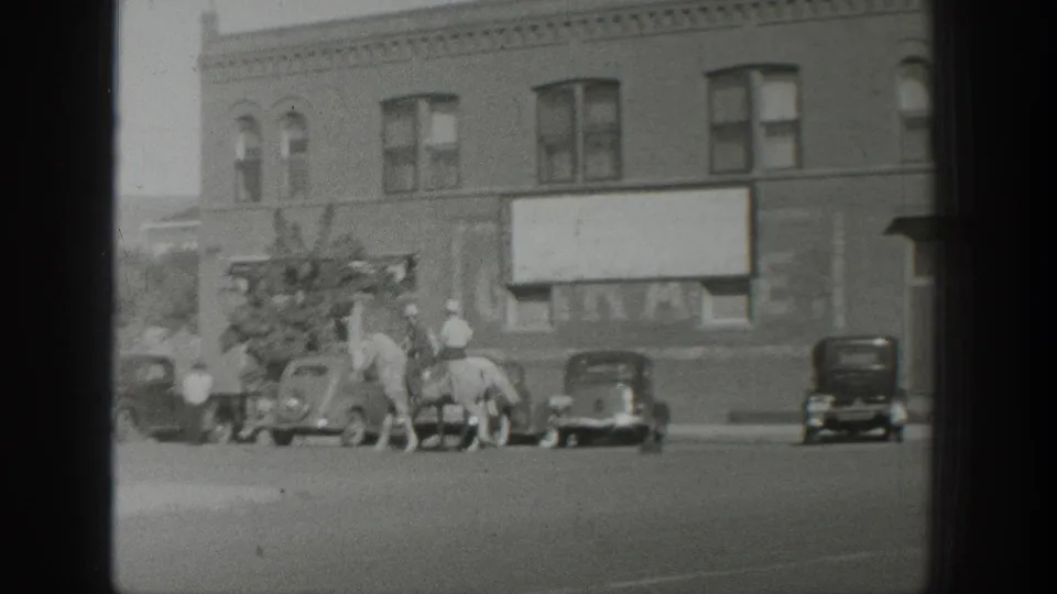 1939 Wyoming street view with mounted riders, pedestrians, parked automobiles, and a large blank sign on a brick building.