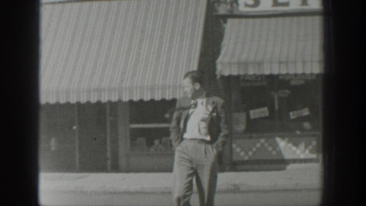 Man in a suit standing on a sidewalk beside storefronts with striped awnings.