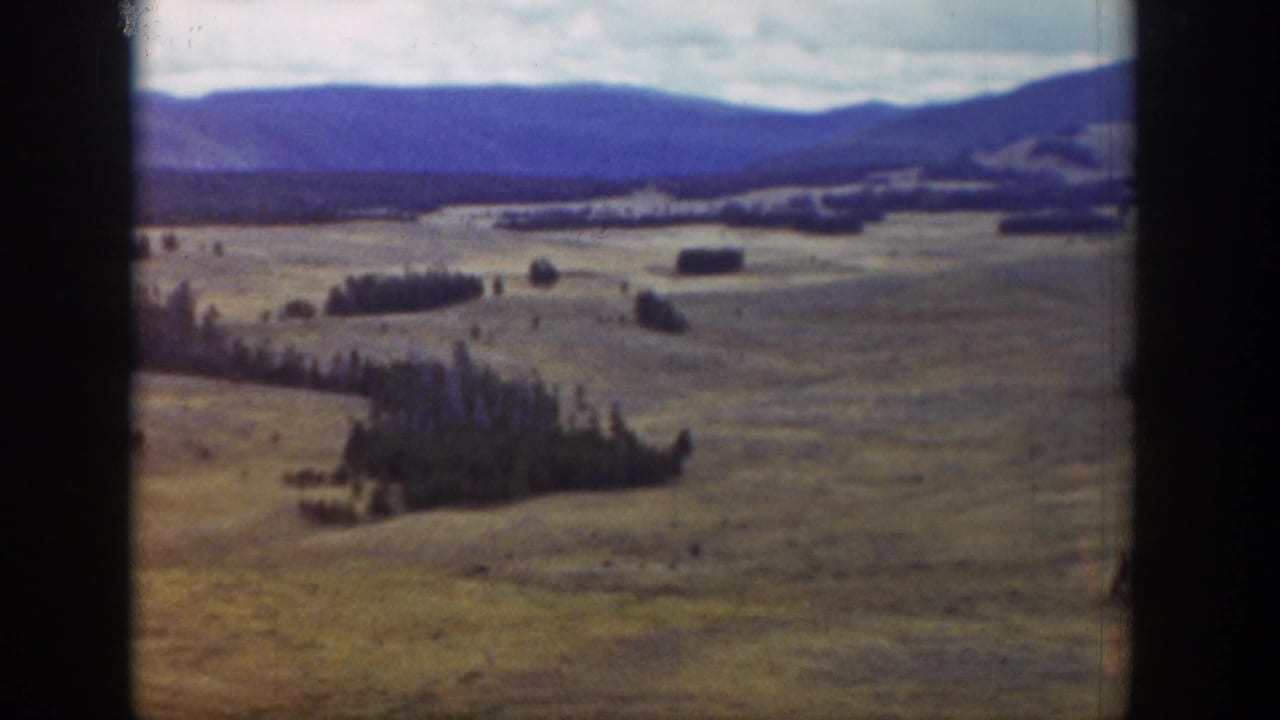 Broad valley landscape with fields, tree stands, distant ridges, and a cloudy sky.