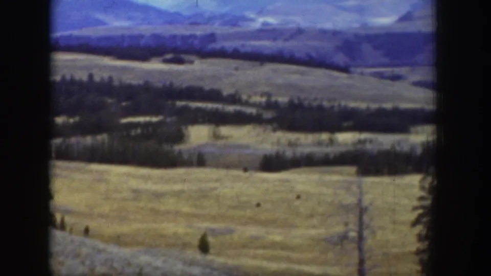 Wide 8mm view of Wyoming grassland with scattered evergreens, distant mountains, and visible film-frame borders.