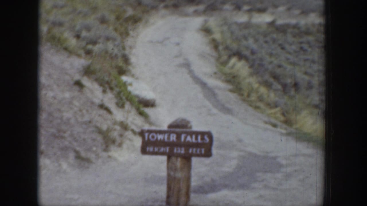 1939 Wyoming 8mm frame showing a Tower Falls sign near a pale dirt path on rugged, sparsely vegetated ground.