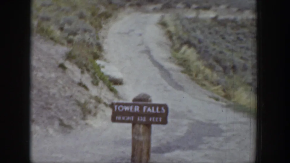 1939 Wyoming 8mm frame showing a Tower Falls sign near a pale dirt path on rugged, sparsely vegetated ground.