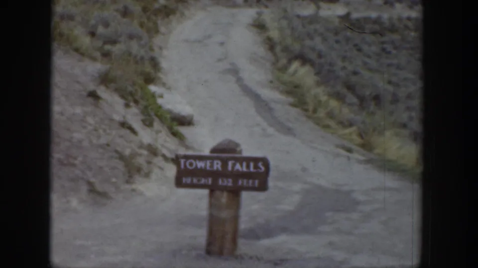 1939 Wyoming home-movie frame with the Tower Falls sign in front of a winding dirt path and dry, rocky hillside.