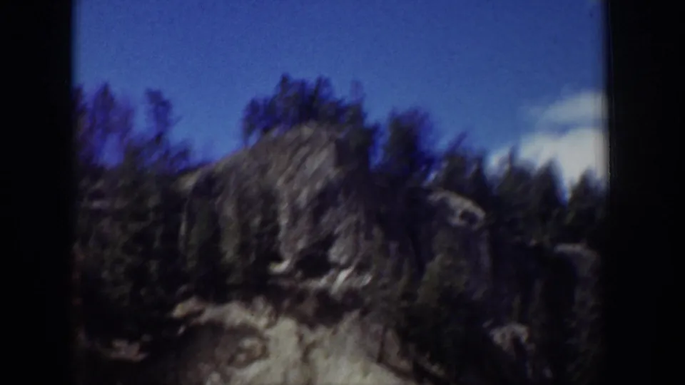1939 Wyoming 8mm frame looking toward a rocky outcrop, trees, and blue sky after the sign view.