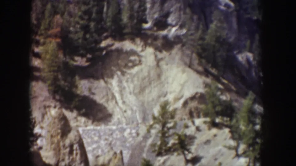 1939 Wyoming home-movie frame showing a pale cliff face, dark tree shadows, and vegetation near Tower Falls.