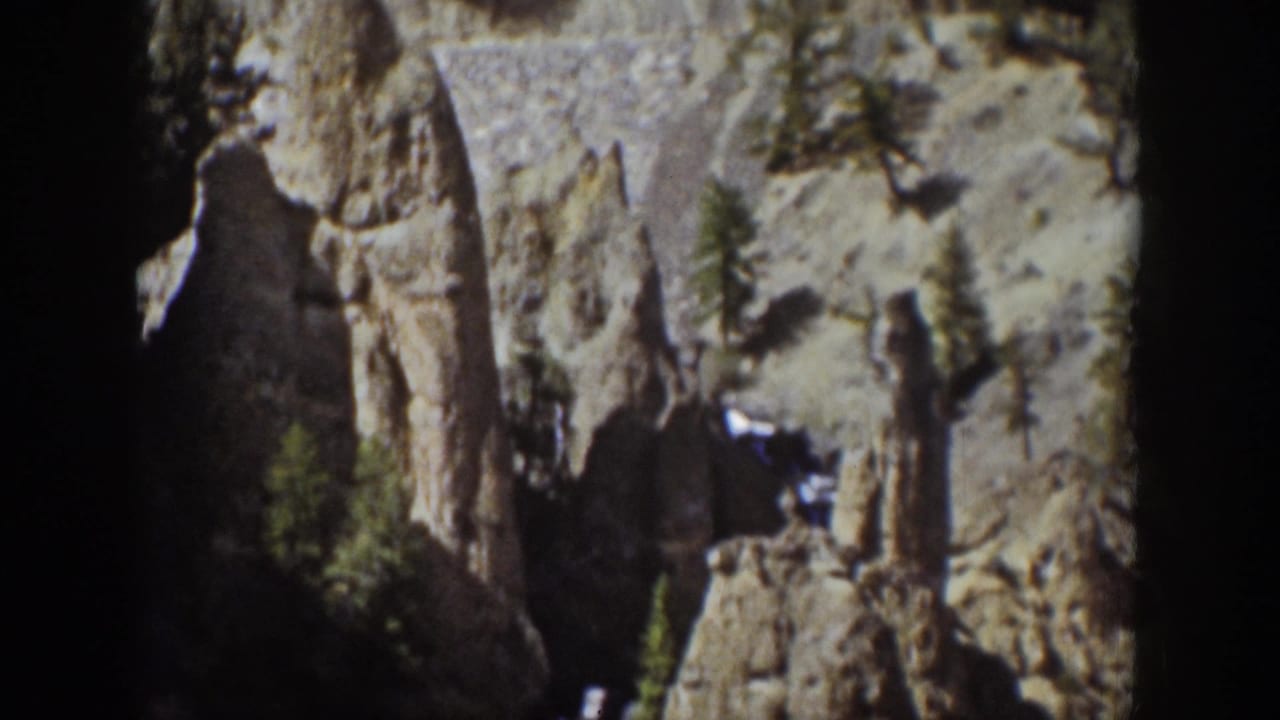 1939 Wyoming 8mm frame with rugged cliff columns, scattered conifers, and the first glimpse of a narrow fall in shadow.