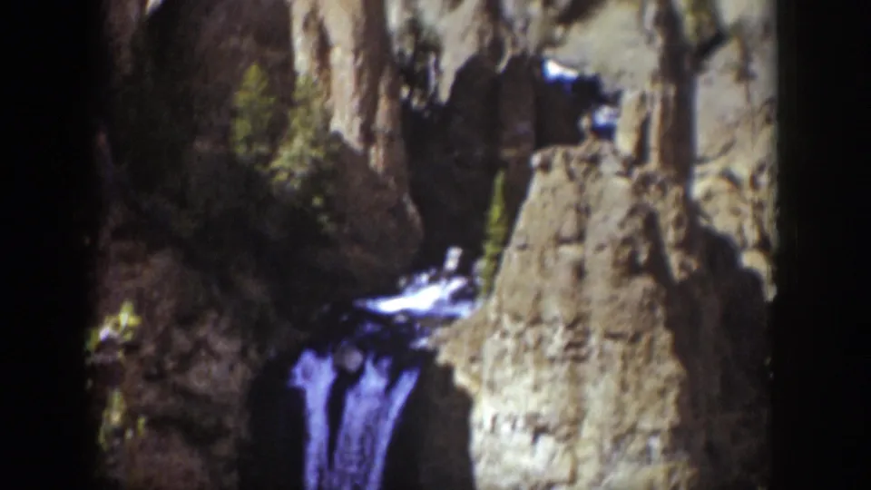 1939 Wyoming 8mm frame showing a purple-blue waterfall dropping through a rocky ravine beneath sunlit cliffs.