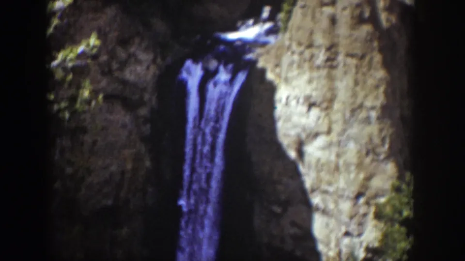 1939 Wyoming 8mm frame centered on the narrow waterfall, with dark ravine rock and a bright cliff face to the side.
