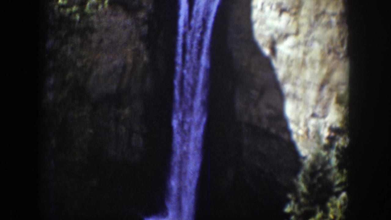 1939 Wyoming 8mm frame showing a narrow waterfall descending along a cliff with evergreen growth and heavy shadowed film edges.