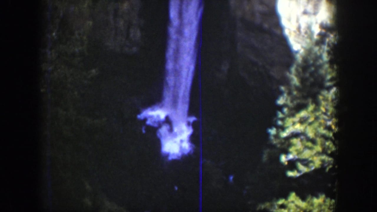 Waterfall plume falling against a dark cliff with trees at the edge.