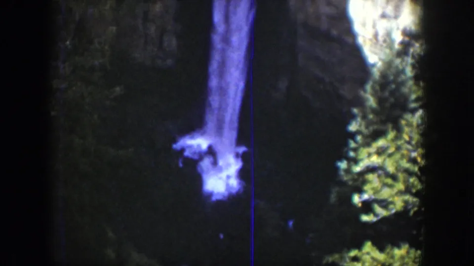1939 Wyoming 8mm frame showing the waterfall from a closer angle, with a bright plume against dark rock and nearby evergreens.