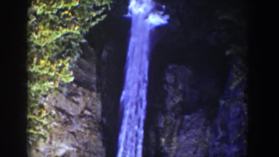 1939 Wyoming 8mm frame showing a side view of the waterfall framed by cliff vegetation, dark rock, and blue-tinted film color.