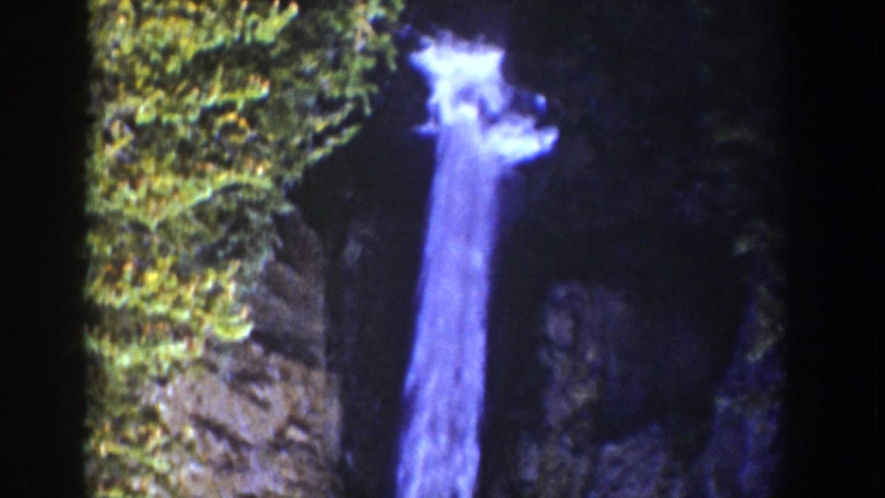 1939 Wyoming 8mm frame showing a bright waterfall dropping through shadowed rock, with mossy cliff surfaces and soft home-movie focus.