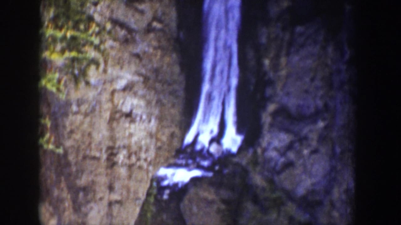 1939 Wyoming 8mm frame with a luminous waterfall against a vertical rock face, framed tightly in dim canyon-like light.