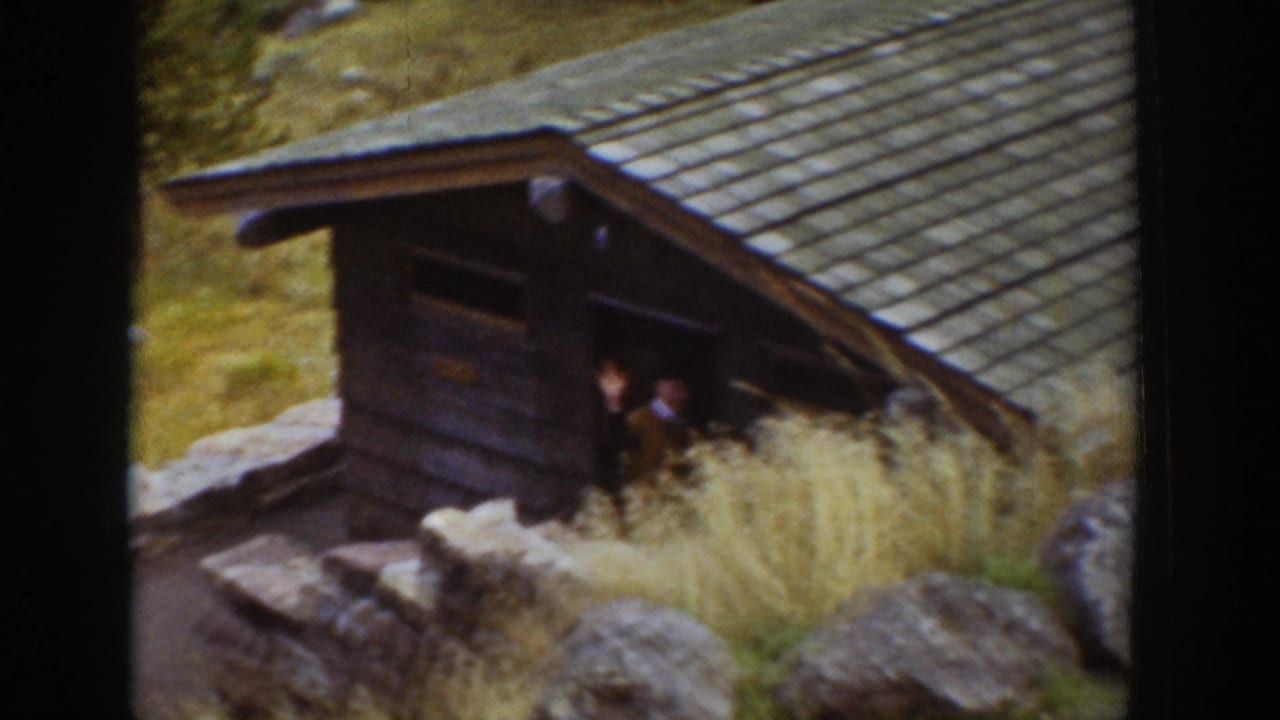 1939 Wyoming 8mm frame showing a man at a rustic cabin doorway with rocks, grass, and a sloped roof visible.