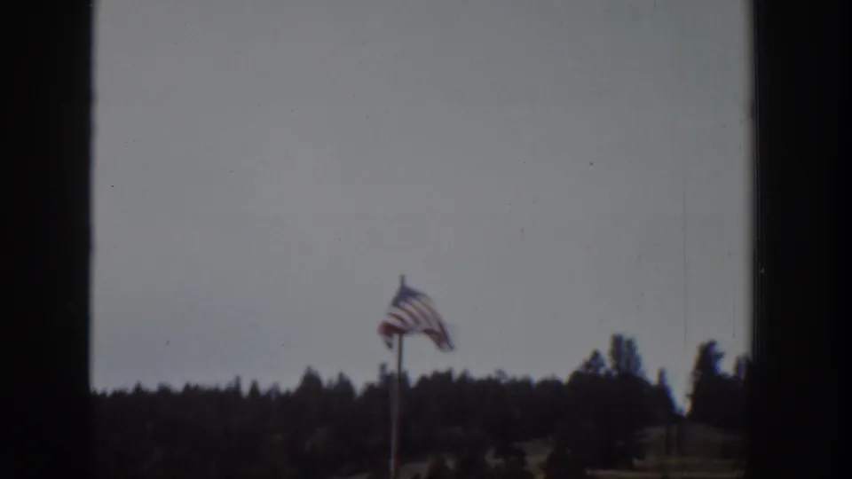 1939 Wyoming home-movie view of an American flag flying above a dark tree line under a cloudy sky.