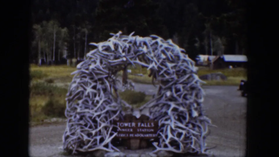 1939 Wyoming 8mm frame showing a white antler arch at the Tower Falls Ranger Station entrance with cabins and forest behind it.