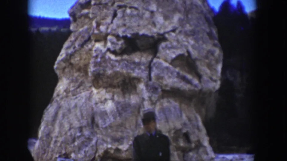 A closer 1939 Wyoming frame shows the craggy rock face filling most of the view, with the visitor low in the foreground.