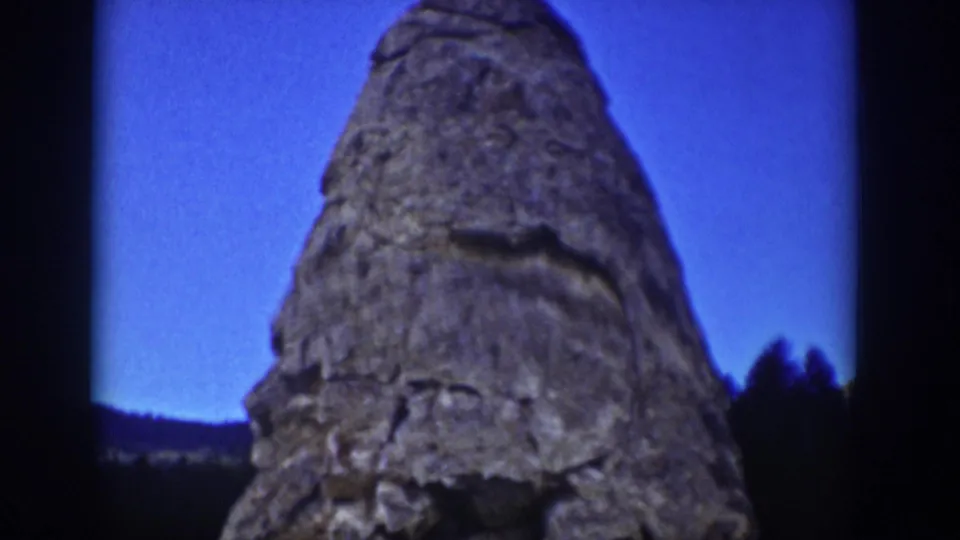 The final frame centers the towering rock formation against blue sky, with distant tree line and dark film border visible.