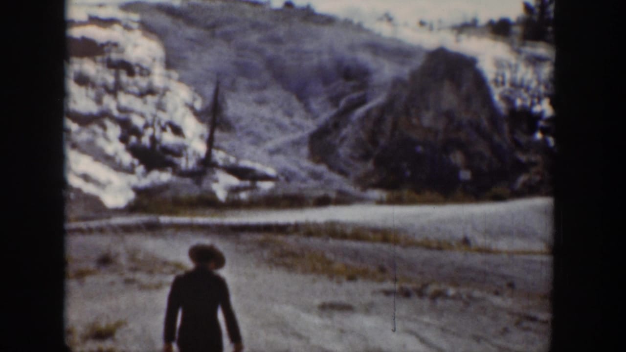 1939 Wyoming 8mm frame showing a woman in a dark coat and brimmed hat walking near a snow-lined mountain road.