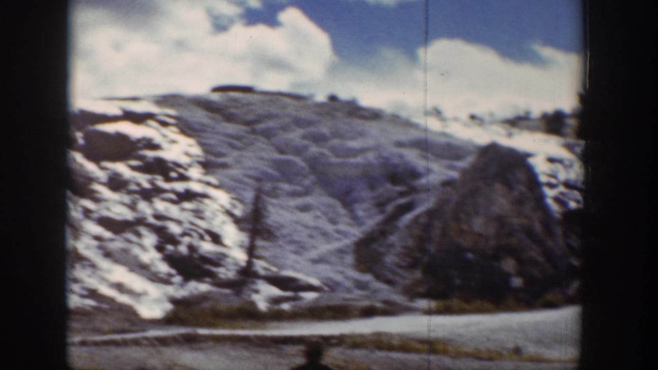 1939 Wyoming 8mm frame looking across a snow-dusted mountain slope beside a valley road under clouds.
