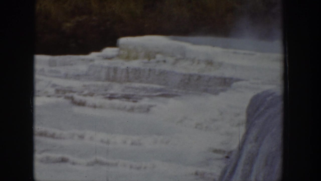 1939 Wyoming 8mm frame of tiered ice along a frozen river or waterfall, with dark winter trees in the background.