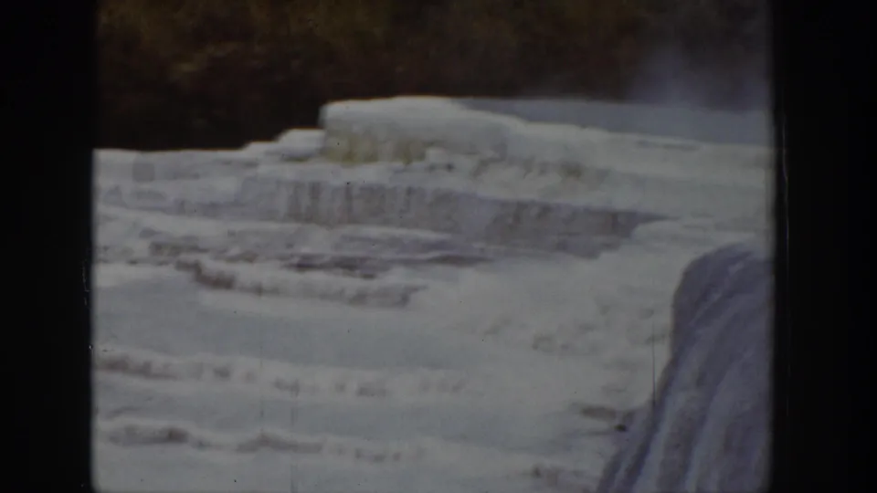 1939 Wyoming 8mm frame of tiered ice along a frozen river or waterfall, with dark winter trees in the background.