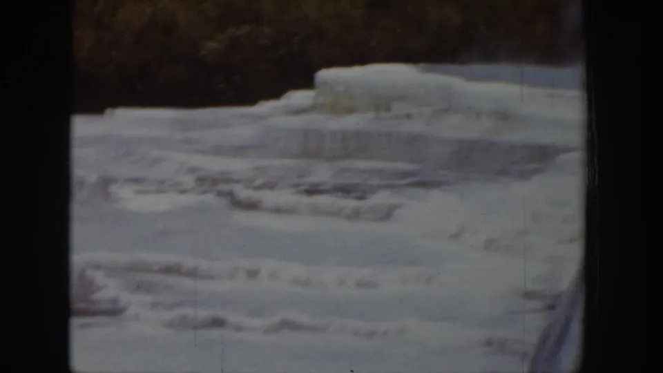 1939 Wyoming 8mm frame showing broad frozen river ice, stepped shelves, and a dark wooded bank beyond.