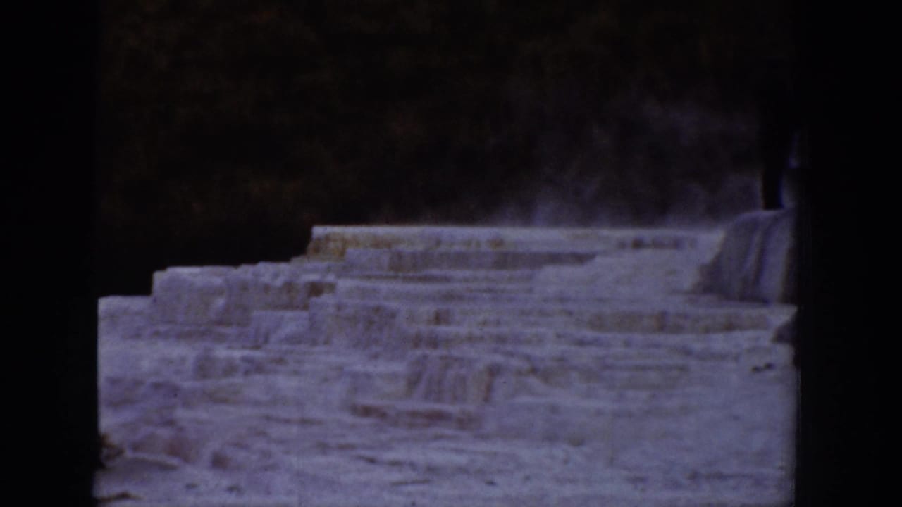 1939 Wyoming 8mm frame showing a pale terraced geothermal waterfall or mineral formation with steam rising and dark film borders.
