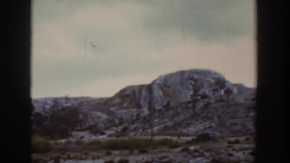 1939 Wyoming 8mm frame showing a rocky hill, sparse vegetation, pale sky, and dark film edge from a home-movie travel sequence.