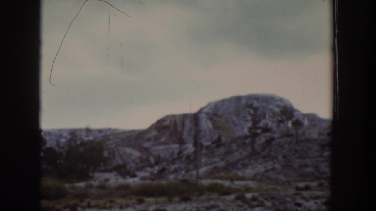1939 Wyoming home-movie frame showing a rocky hillside and sparse trees viewed through a dark window divider.