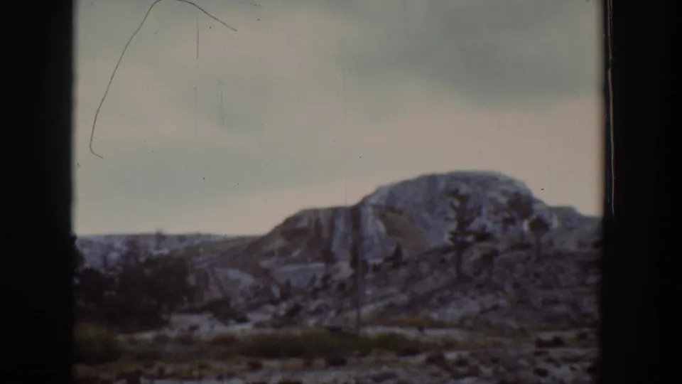 1939 Wyoming home-movie frame showing a rocky hillside and sparse trees viewed through a dark window divider.