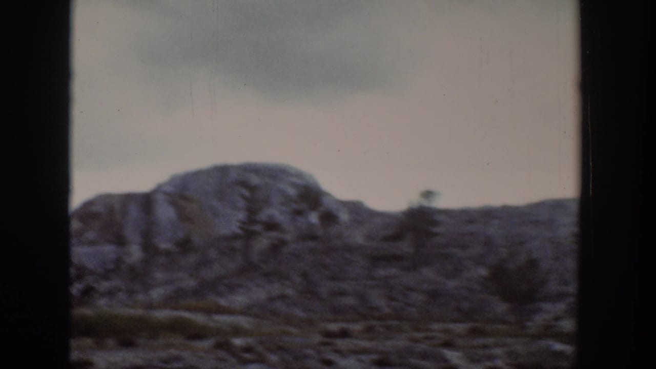 1939 Wyoming landscape view of a low rocky mountain slope, sparse trees and muted sky through a vehicle or window frame.