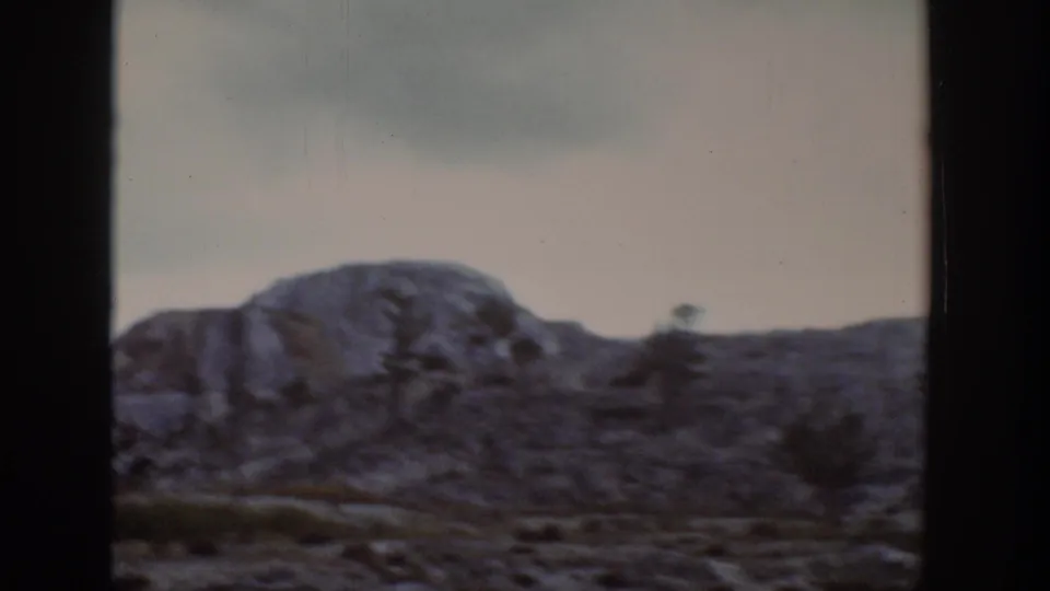 1939 Wyoming landscape view of a low rocky mountain slope, sparse trees and muted sky through a vehicle or window frame.