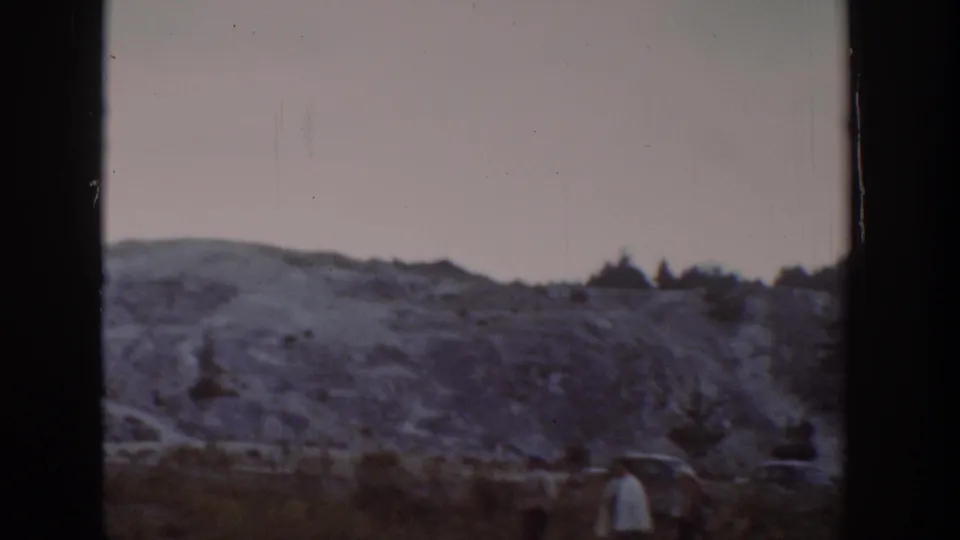 1939 Wyoming landscape frame with a rocky hillside, scrub vegetation and distant roadside figures near the lower right.