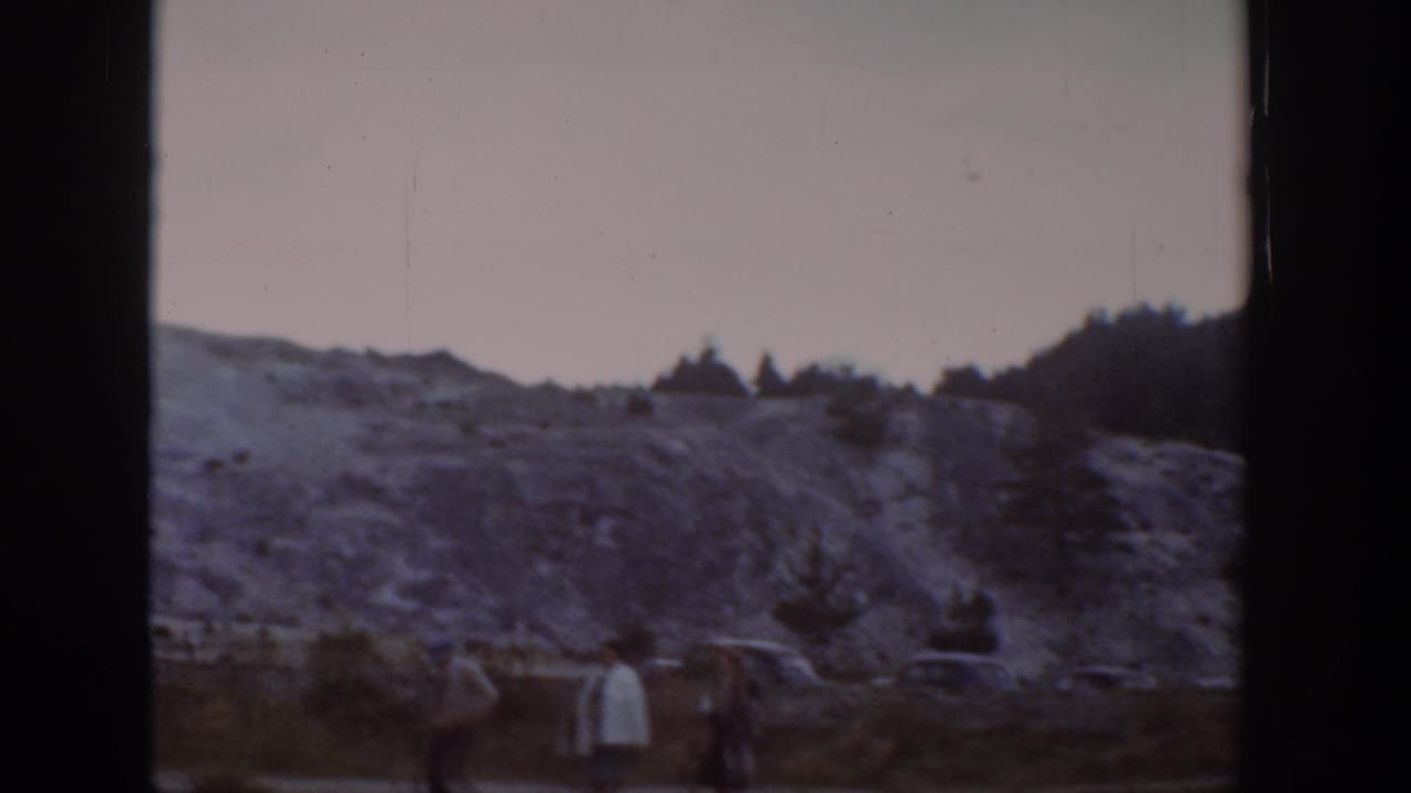 1939 Wyoming home-movie frame showing distant visitors near a pale rocky slope and low wooded hills.