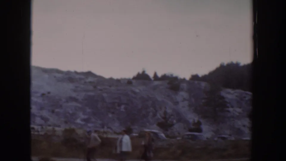 1939 Wyoming home-movie frame showing distant visitors near a pale rocky slope and low wooded hills.