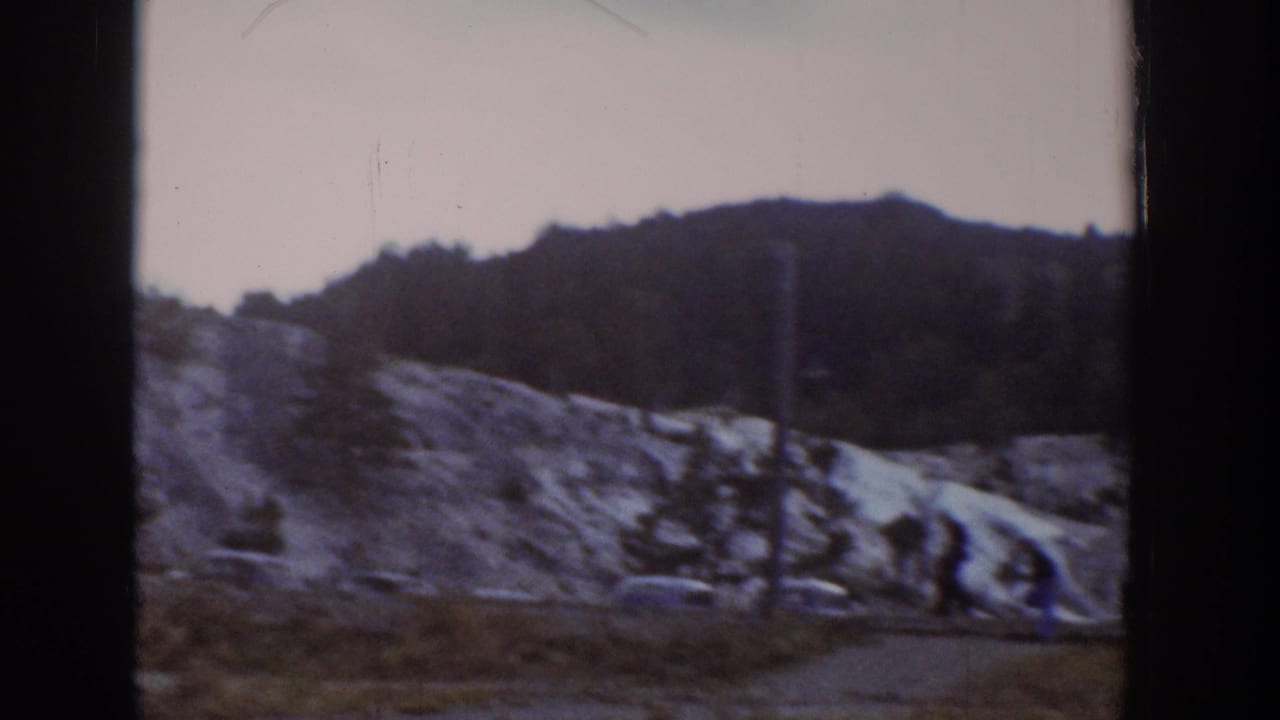 Rocky hillside beside a dirt path with parked cars and trees in the distance.