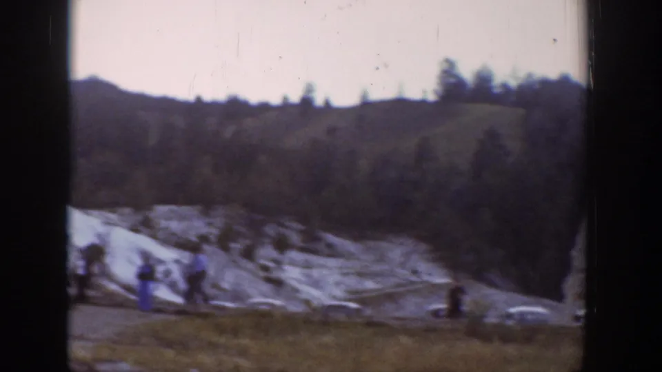 1939 Wyoming 8mm frame showing visitors walking near pale rock outcrops below a tree-lined hillside.