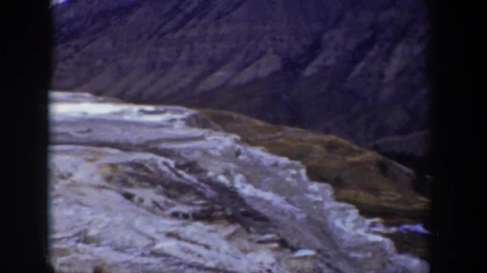Wyoming mountain landscape frame with a pale, eroded rock surface and darker ridged terrain in the background.