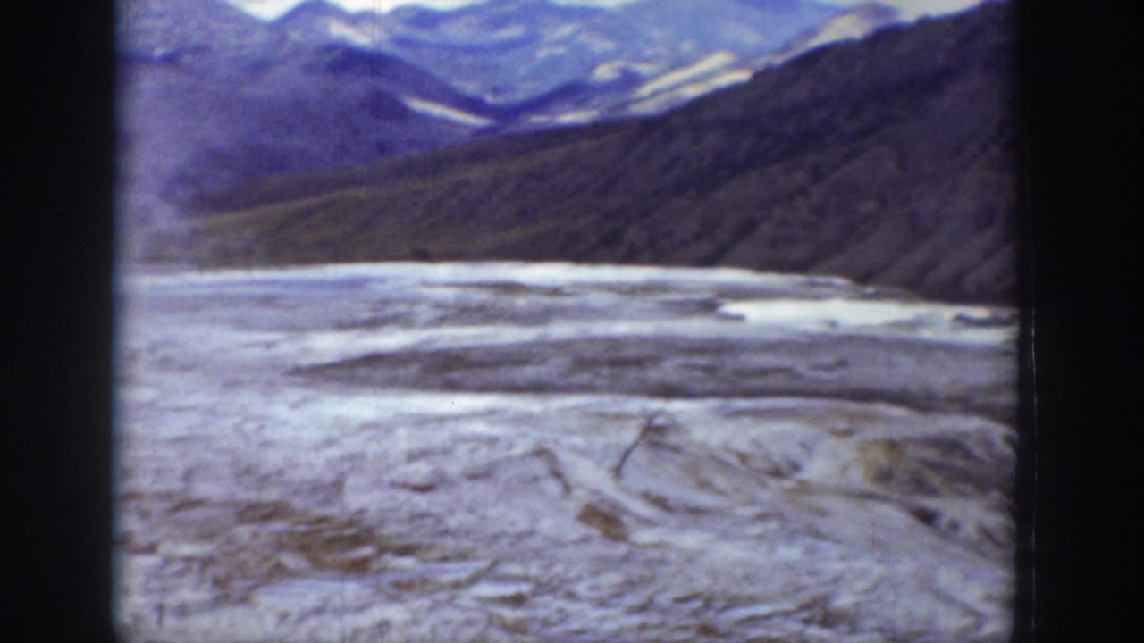 1939 Wyoming 8mm frame showing a snow-covered or frozen valley floor beneath dark mountain slopes and distant pale peaks.