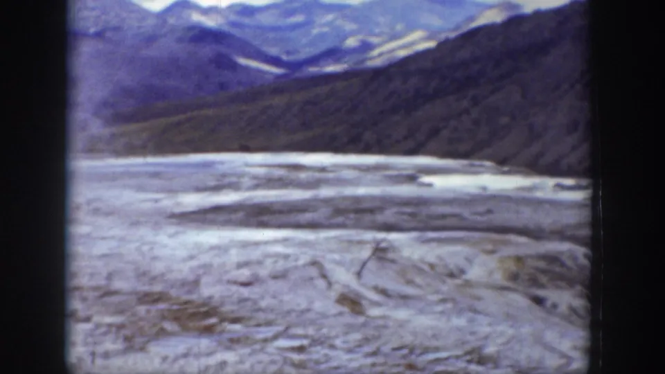 1939 Wyoming 8mm frame showing a snow-covered or frozen valley floor beneath dark mountain slopes and distant pale peaks.