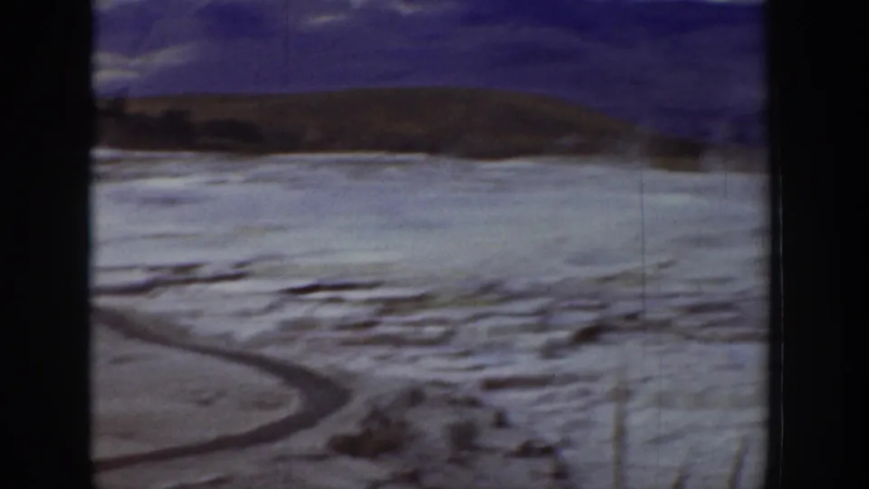 1939 Wyoming 8mm frame showing snowy open ground, a winding dark channel, low ridge, and blurred winter mountains beyond.