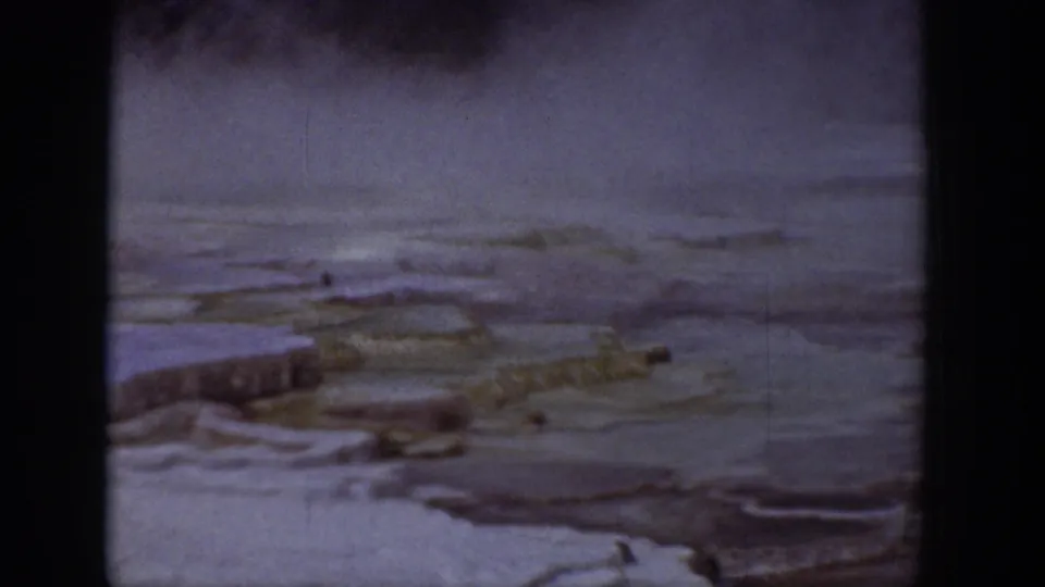 1939 Wyoming 8mm frame where mist or steam appears over icy terrain with low ridges, dark patches, and a muted mountain backdrop.