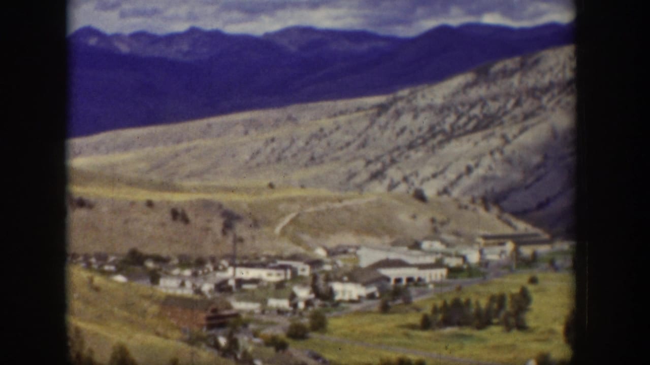 1939 Wyoming 8mm frame showing a small valley settlement below rugged hills, with scattered trees, roads, and distant mountain ridges.