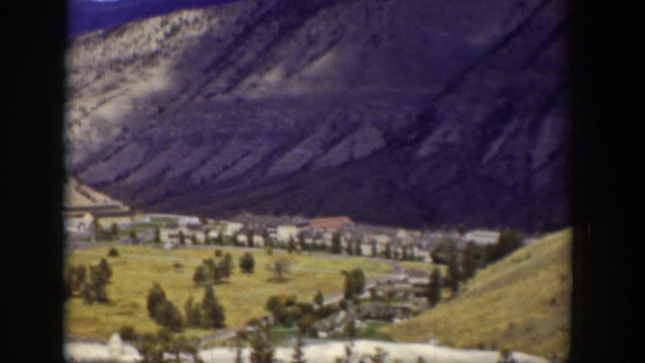 Cluster of buildings and trees at the base of steep rocky hills.