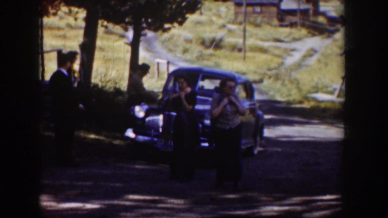 1939 Wyoming home-movie frame showing several people beside a dark sedan on a rural road with hills beyond.