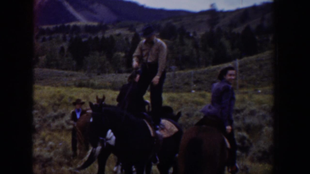Riders and horses stand in an open grassy hillside landscape.